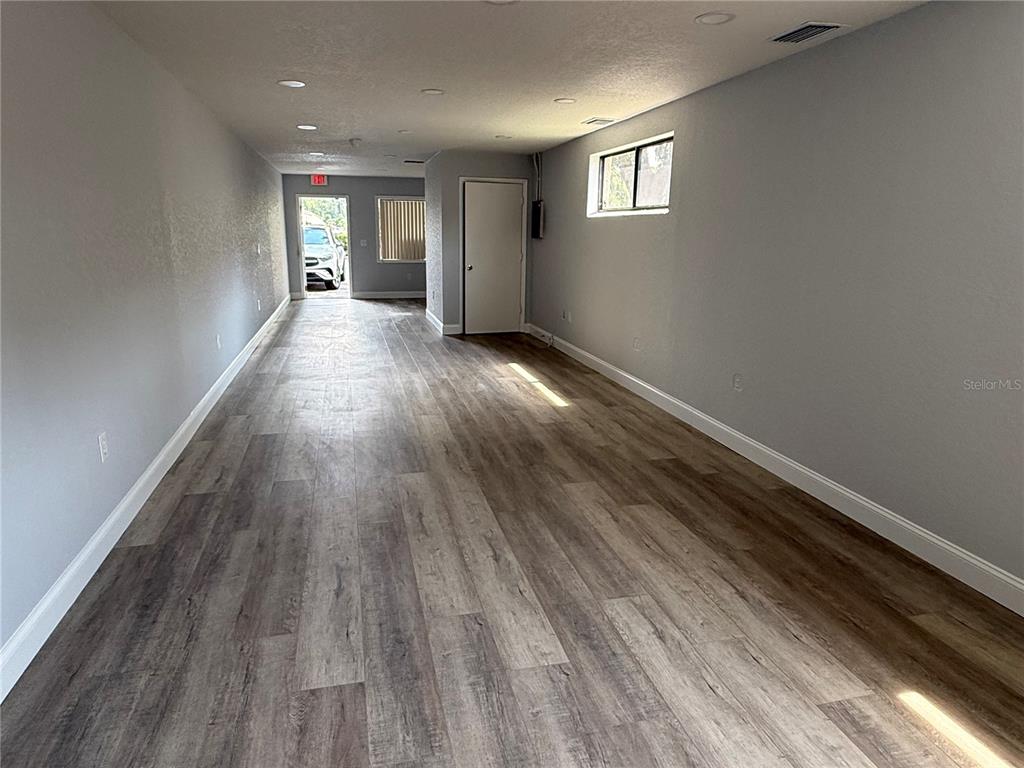 A long, empty room features gray walls, wood-look flooring, recessed lighting, and a rear exit — 15 UTILITY DRIVE UNIT A, PALM COAST, FL