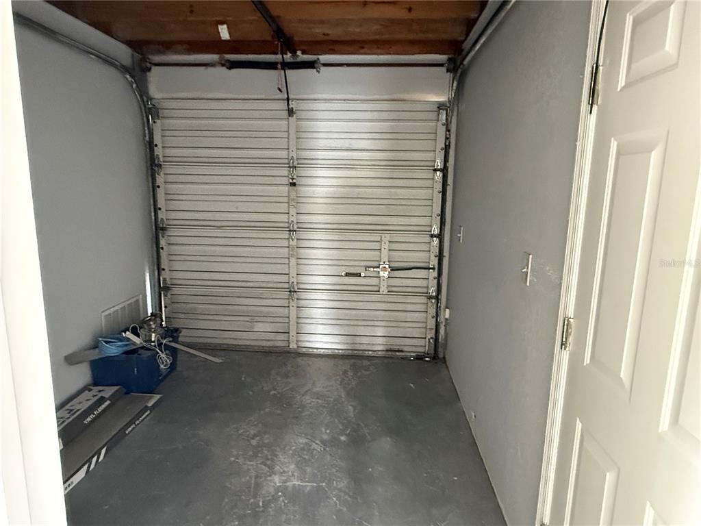 A small garage with a metal roll-up door, gray walls, and concrete flooring — 15 UTILITY DRIVE UNIT A, PALM COAST, FL