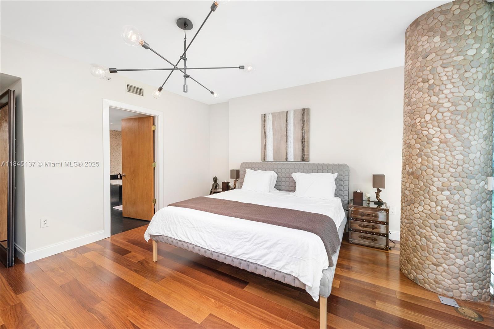A bedroom features a gray upholstered bed, hardwood floors, a stone column, and modern lighting — 101 20th St # 1706, Miami Beach FL 33139, MIAMI BEACH, FL
