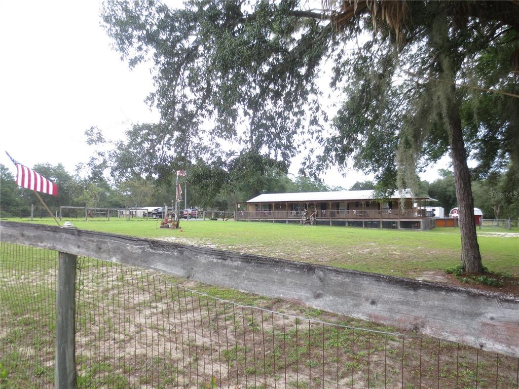A wide view of a single-story house with a long porch behind a wooden fence — 5995 SE 183RD AVENUE ROAD, OCKLAWAHA, FL