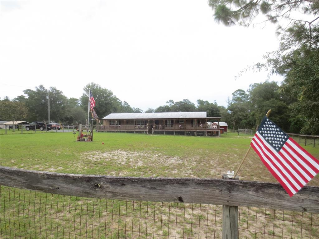 A single-story house with a large wooden porch sits on a grassy rural lot — 5995 SE 183RD AVENUE ROAD, OCKLAWAHA, FL