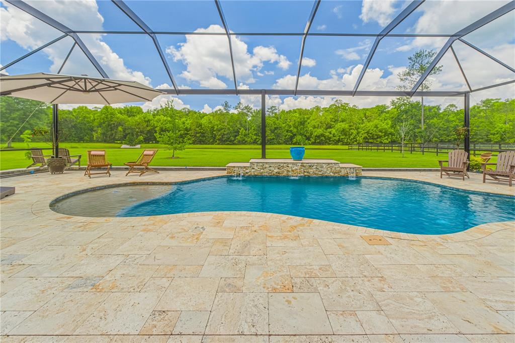 A screened-in pool patio features stone pavers, a water feature, and a large grassy yard — 121 ASHTON OAKS DRIVE, ST AUGUSTINE, FL