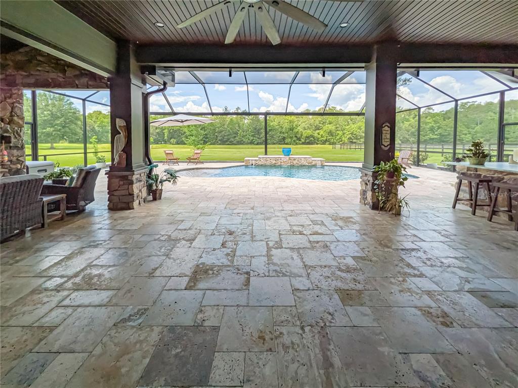 A covered stone patio overlooks a screened-in swimming pool and a large grassy backyard — 121 ASHTON OAKS DRIVE, ST AUGUSTINE, FL