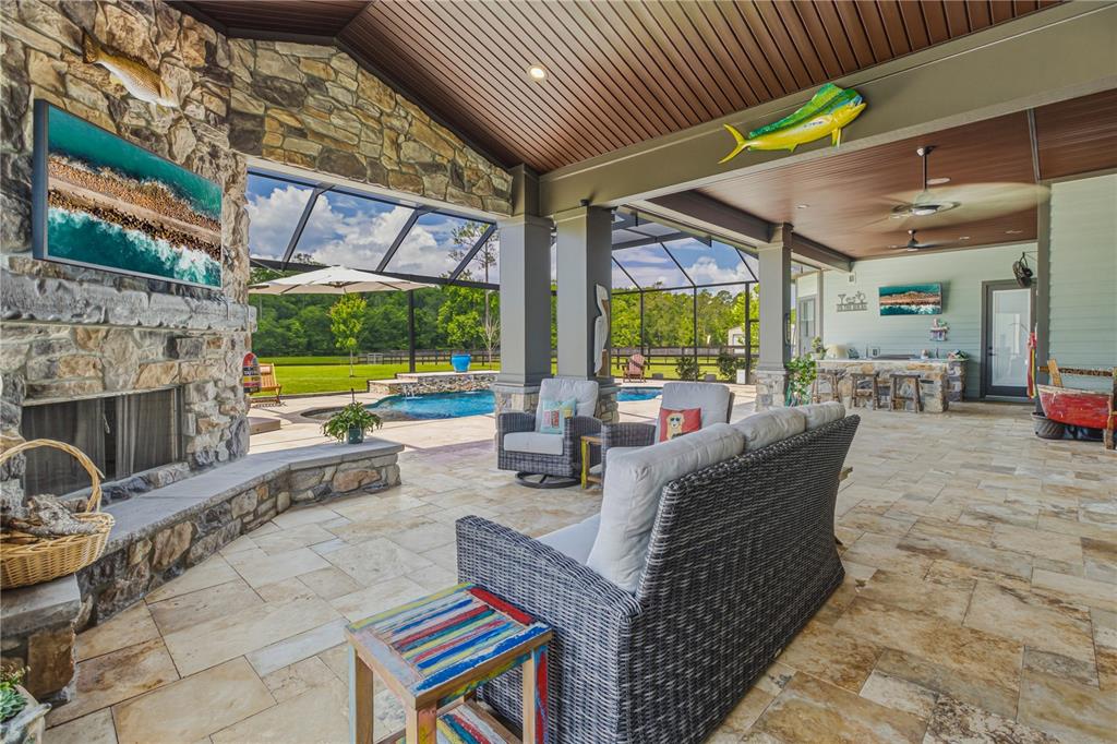 A covered outdoor patio features a stone fireplace, wicker furniture, and a view of a pool — 121 ASHTON OAKS DRIVE, ST AUGUSTINE, FL