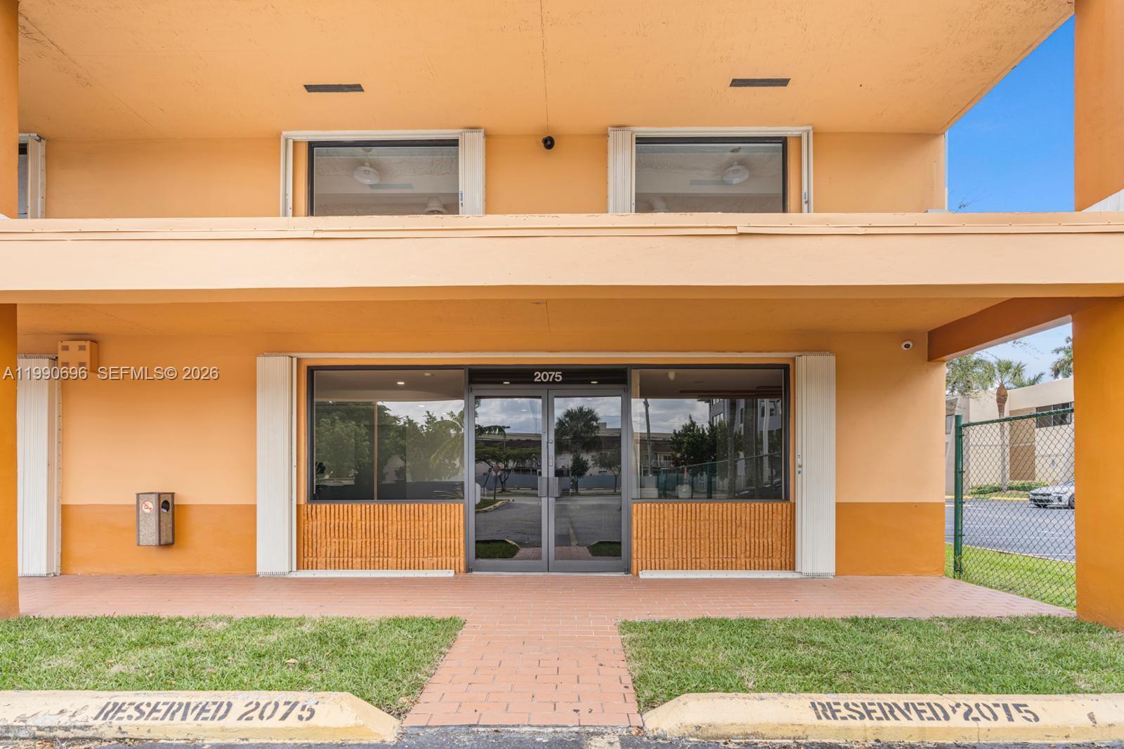 The exterior of a commercial building features an orange facade with a glass entrance door — 2075 W 76th St # 1, Hialeah FL 33016, HIALEAH, FL