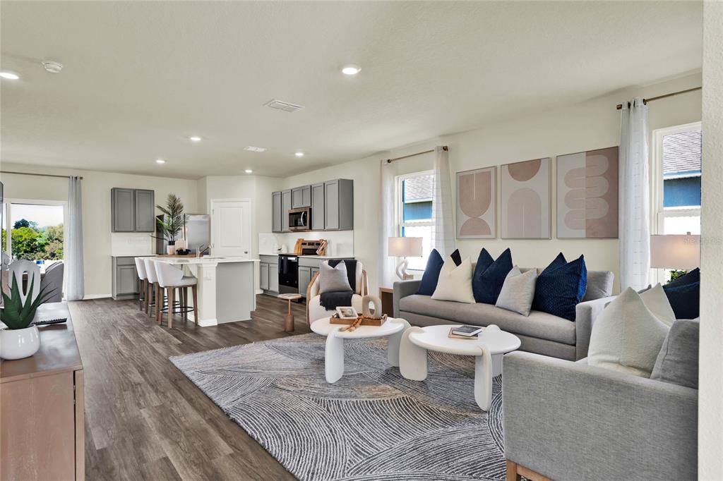 An open-concept living room and kitchen featuring grey cabinetry, wood-look flooring, and a large area rug — 5150 MARSHELDER STREET, APOPKA, FL