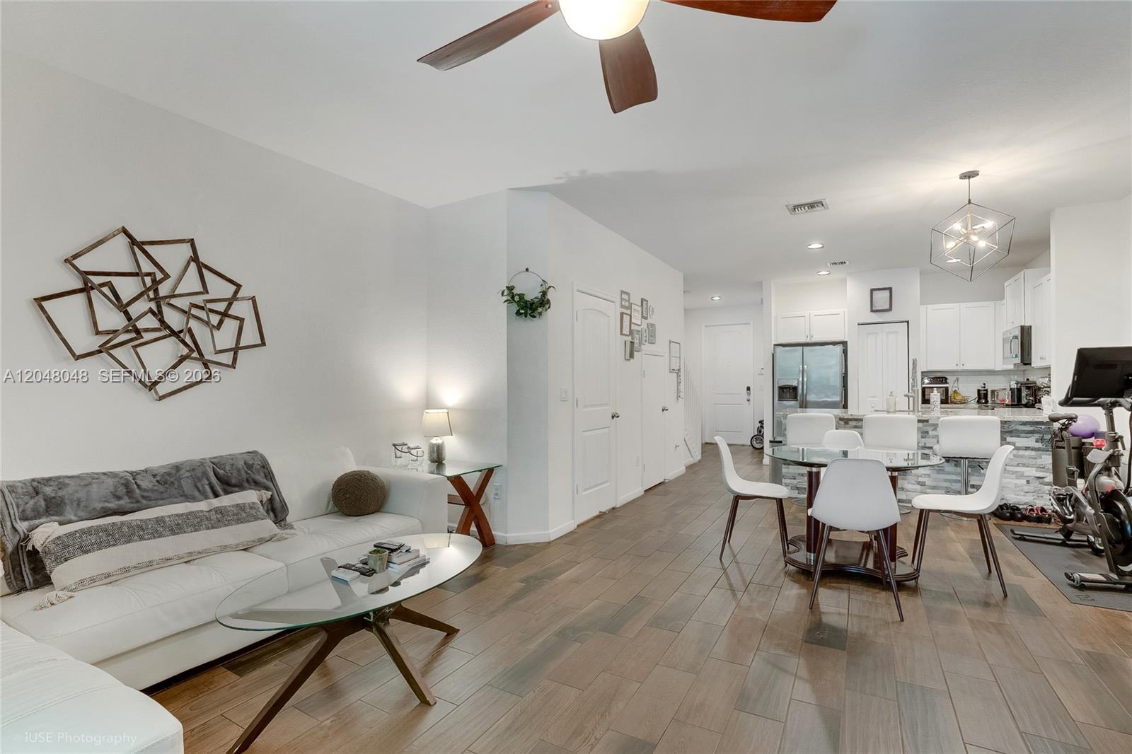 An open-concept living and dining area features white walls, wood-look tile flooring, and modern furniture — 355 SE 1st Dr, Deerfield Beach FL 33441, DEERFIELD BEACH, FL