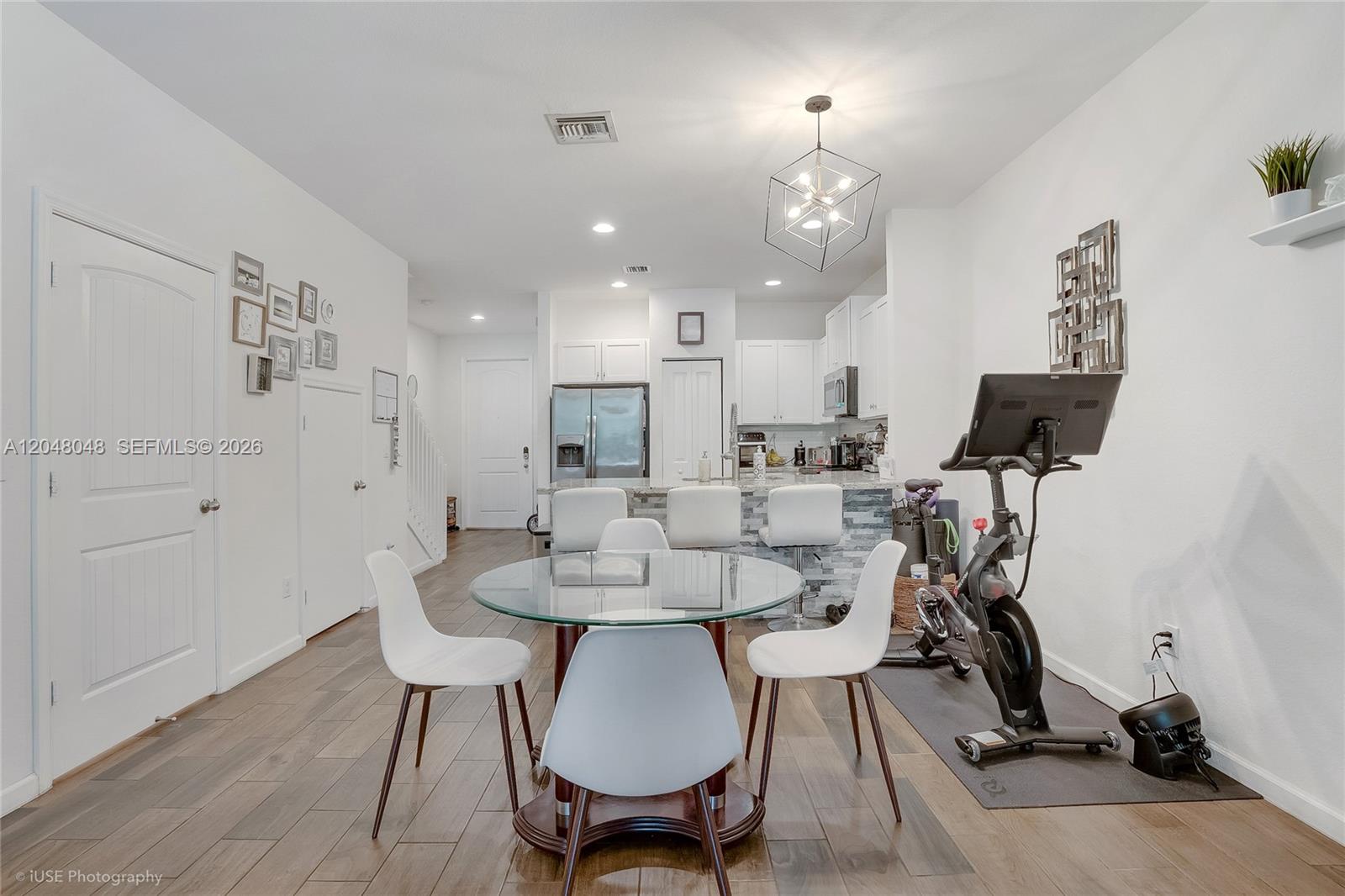 A dining area with a glass table and exercise bike sits before an open kitchen — 355 SE 1st Dr, Deerfield Beach FL 33441, DEERFIELD BEACH, FL