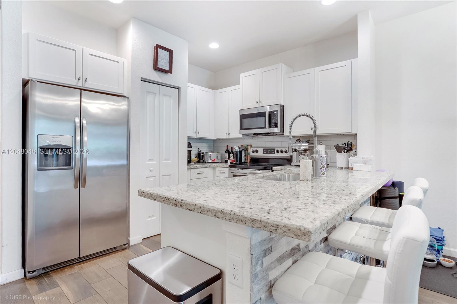 A modern kitchen features white cabinetry, stainless steel appliances, and a granite-topped breakfast bar — 355 SE 1st Dr, Deerfield Beach FL 33441, DEERFIELD BEACH, FL