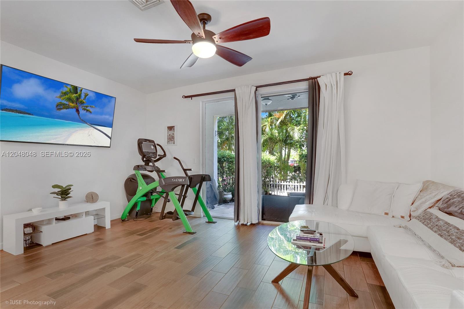 A living room features wood-look tile floors, a white sofa, a glass coffee table, and exercise equipment — 355 SE 1st Dr, Deerfield Beach FL 33441, DEERFIELD BEACH, FL