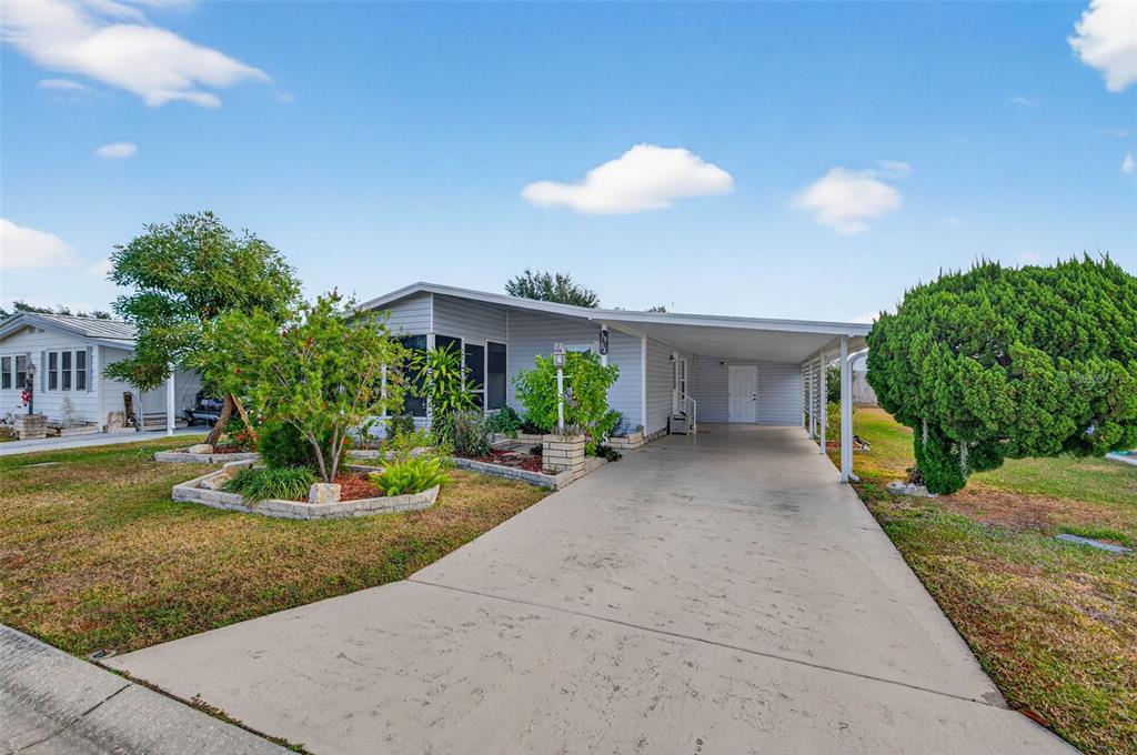 A single-story mobile home with a concrete driveway, carport, and landscaped front yard — 3904 WILLIAM HUME DRIVE, ZEPHYRHILLS, FL