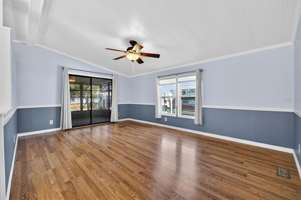 A living room with light blue walls, dark blue wainscoting, wood flooring, and a ceiling fan — 3904 WILLIAM HUME DRIVE, ZEPHYRHILLS, FL