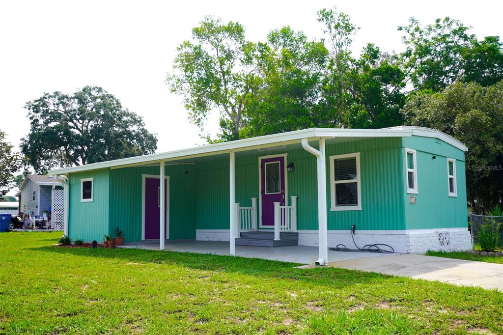 A teal mobile home features a covered carport, purple doors, and a white brick foundation — 8114 WESTERN CIRCLE DRIVE, BROOKSVILLE, FL