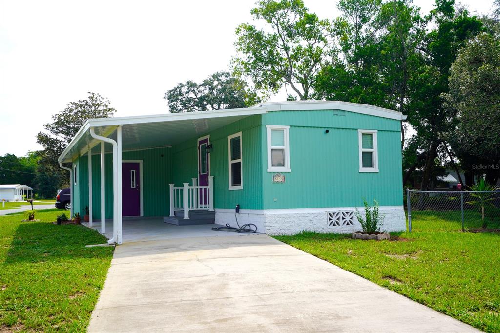 A teal mobile home with a white carport, purple door, and concrete driveway — 8114 WESTERN CIRCLE DRIVE, BROOKSVILLE, FL