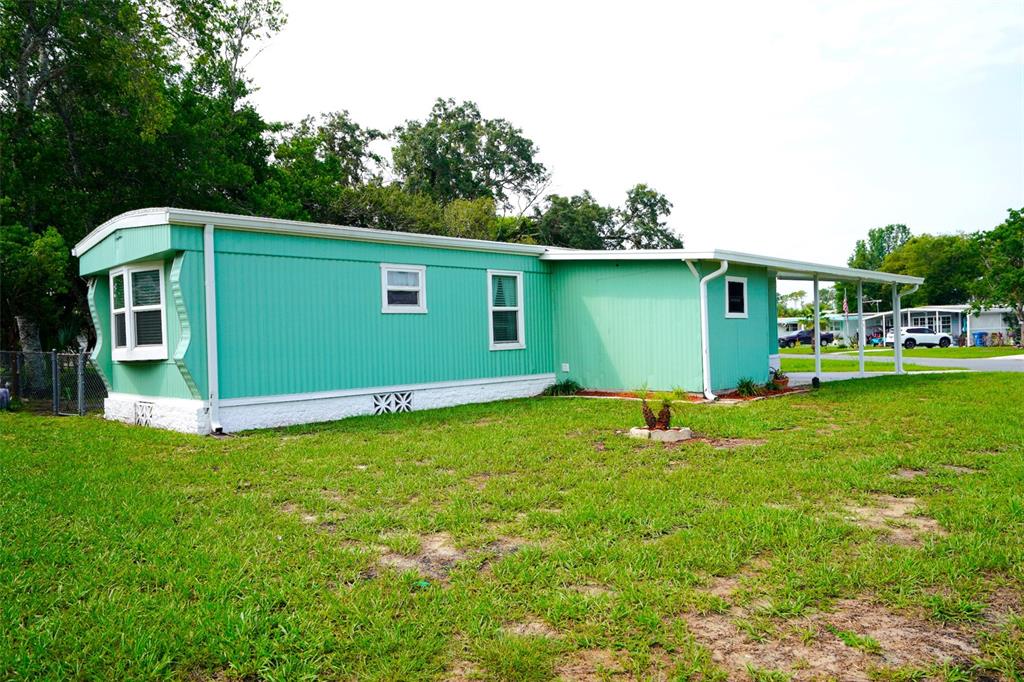 A teal mobile home with a white skirt and a covered carport sits on grass — 8114 WESTERN CIRCLE DRIVE, BROOKSVILLE, FL
