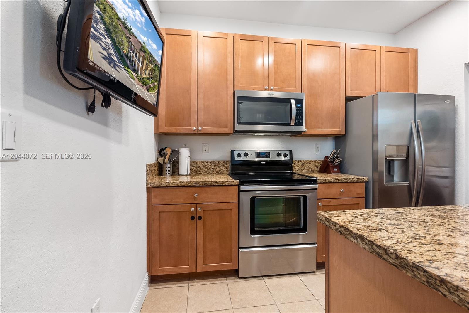 A kitchen features wooden cabinets, granite countertops, stainless steel appliances, and a wall-mounted television — 1119 SW 147th Ave, Pembroke Pines FL 33027, PEMBROKE PINES, FL