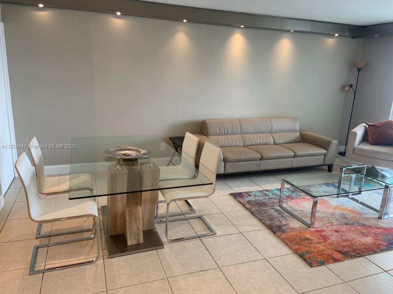 A living and dining area features a glass-top table, beige sofa, and tile flooring — 5151 Collins Ave # 727, Miami Beach FL 33140, MIAMI BEACH, FL