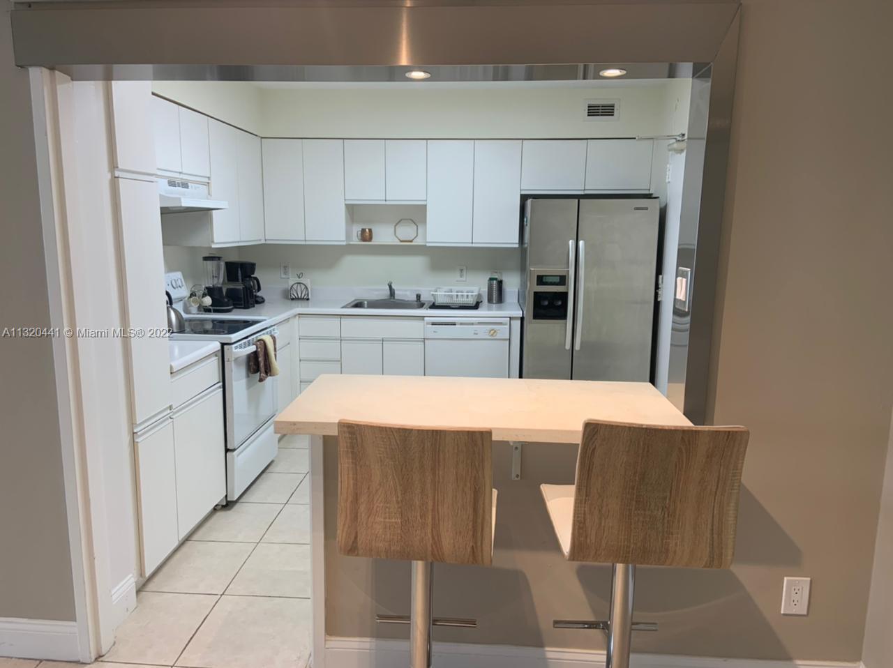 A kitchen features white cabinets, stainless steel appliances, and a breakfast bar with two stools — 5151 Collins Ave # 727, Miami Beach FL 33140, MIAMI BEACH, FL