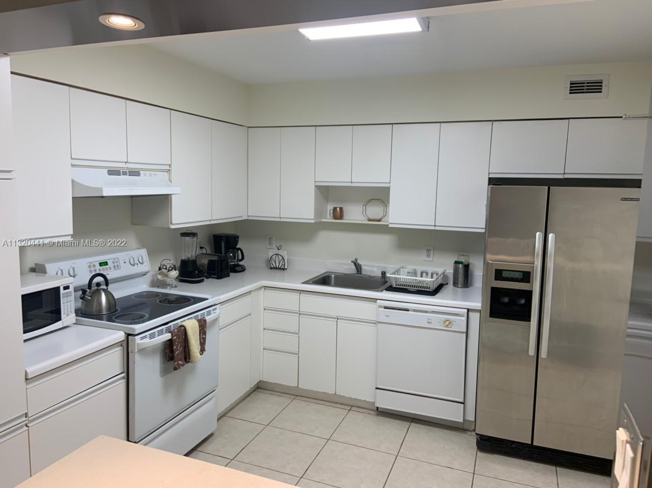 A kitchen features white cabinetry, a stainless steel refrigerator, and a white electric range — 5151 Collins Ave # 727, Miami Beach FL 33140, MIAMI BEACH, FL
