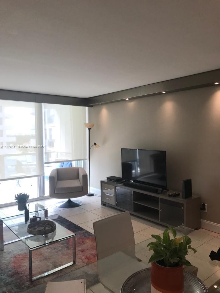 A living room features a television on a console, a gray armchair, and tile flooring — 5151 Collins Ave # 727, Miami Beach FL 33140, MIAMI BEACH, FL