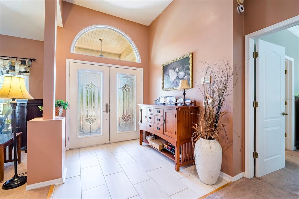 A bright entryway features a double front door, tile flooring, and a wooden console table — 22754 MAGNOLIA TRACE BOULEVARD, LUTZ, FL