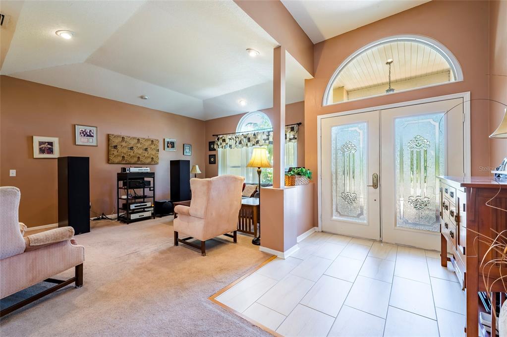 A living room with carpeted floors, a tiled entryway, and double glass-paneled front doors — 22754 MAGNOLIA TRACE BOULEVARD, LUTZ, FL