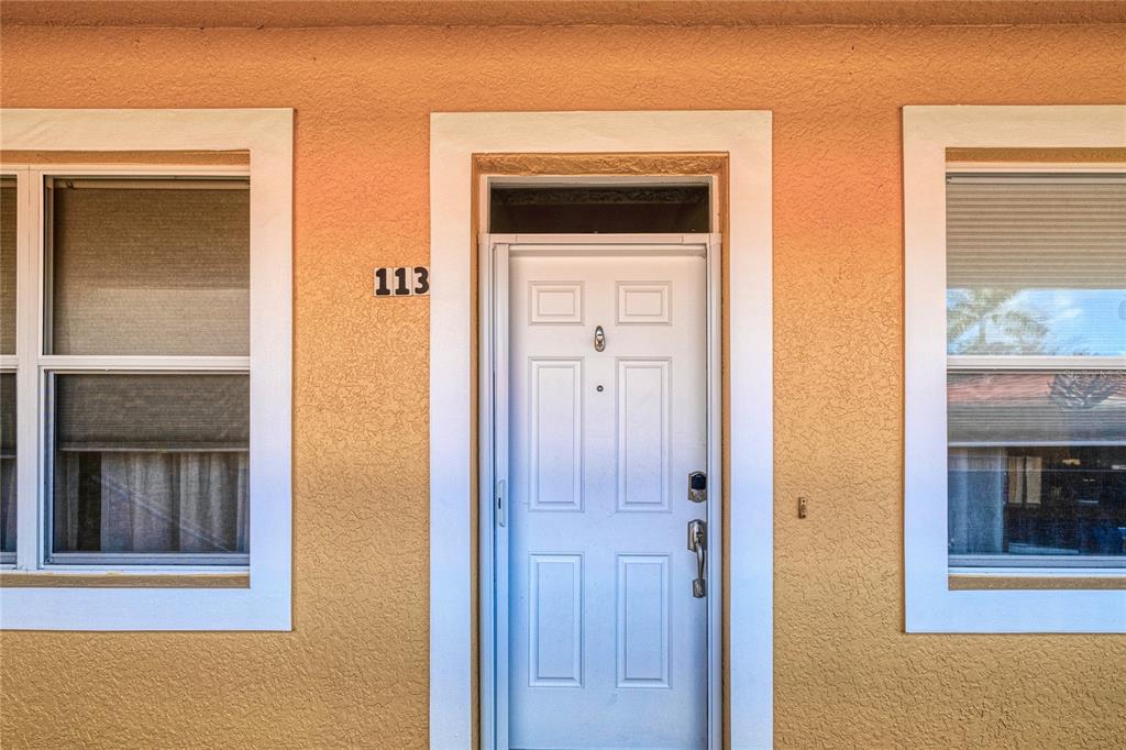 A white front door with the number 113 is flanked by two windows on stucco walls — 3228 PURPLE MARTIN DRIVE UNIT 113, PUNTA GORDA, FL