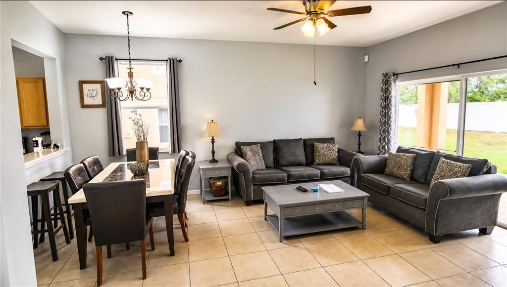 An open-concept living and dining area features tile flooring, gray sofas, and a dining set — 2540 CALABRIA AVENUE, DAVENPORT, FL