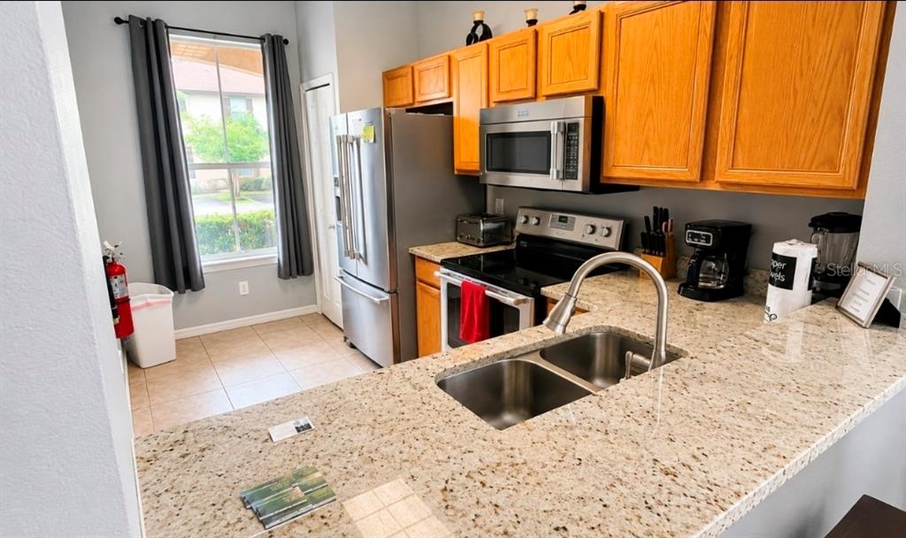 A kitchen features light granite countertops, stainless steel appliances, and honey-oak wooden cabinets — 2540 CALABRIA AVENUE, DAVENPORT, FL