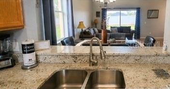A kitchen sink with a gooseneck faucet overlooks a living room with granite countertops — 2540 CALABRIA AVENUE, DAVENPORT, FL