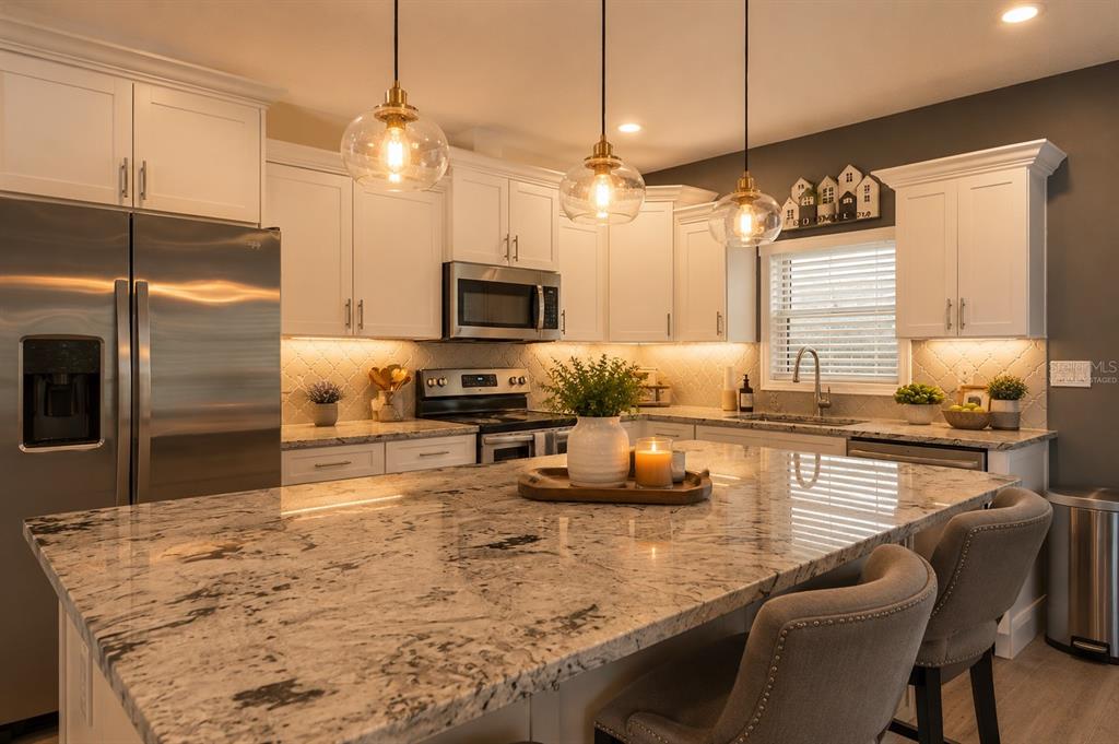 A kitchen with white cabinets, granite countertops, a large island, and three glass pendant lights — 5328 BALDOCK AVENUE, SPRING HILL, FL