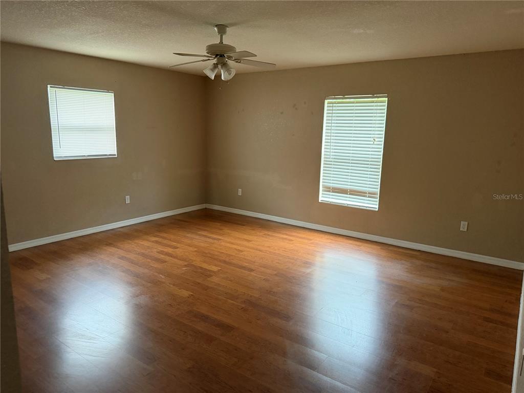 An empty room features light brown walls, wood-look flooring, a ceiling fan, and two windows — 9371 SE 108TH PLACE, BELLEVIEW, FL
