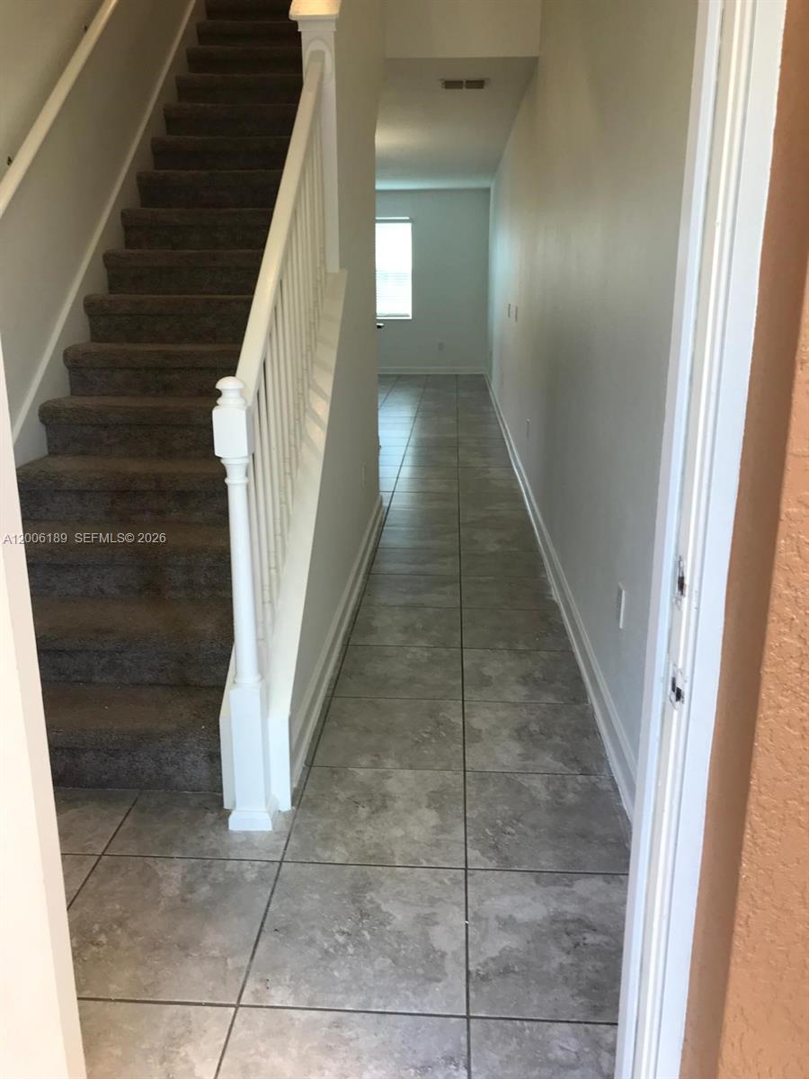 A carpeted staircase with a white railing sits beside a tiled hallway leading to a window — 3348 RODRICK CIR, Orlando FL 32824, ORLANDO, FL
