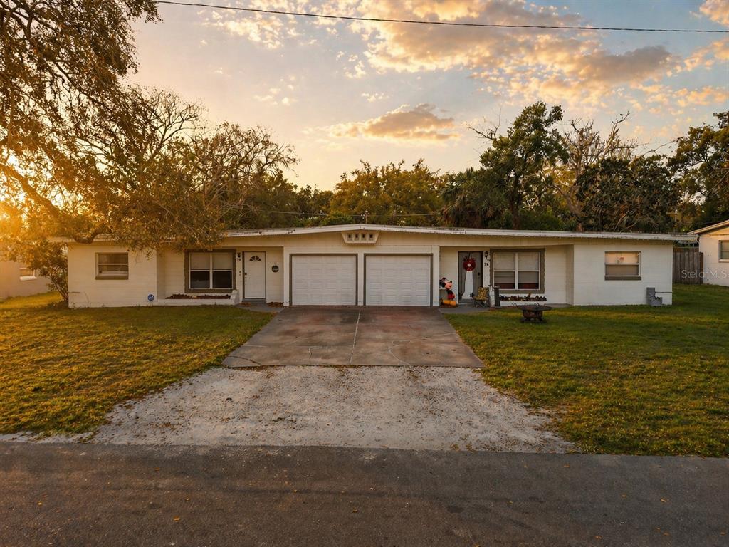A single-story duplex with two garage doors, white siding, and a concrete driveway at sunset — 70-76 GRIGGS AVENUE, CASSELBERRY, FL