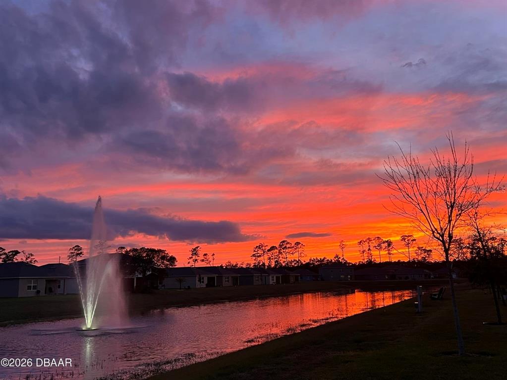 A pond with a fountain reflects a vibrant sunset behind a row of suburban houses — 1346 MIDDLE LAKE DRIVE, ORMOND BEACH, FL