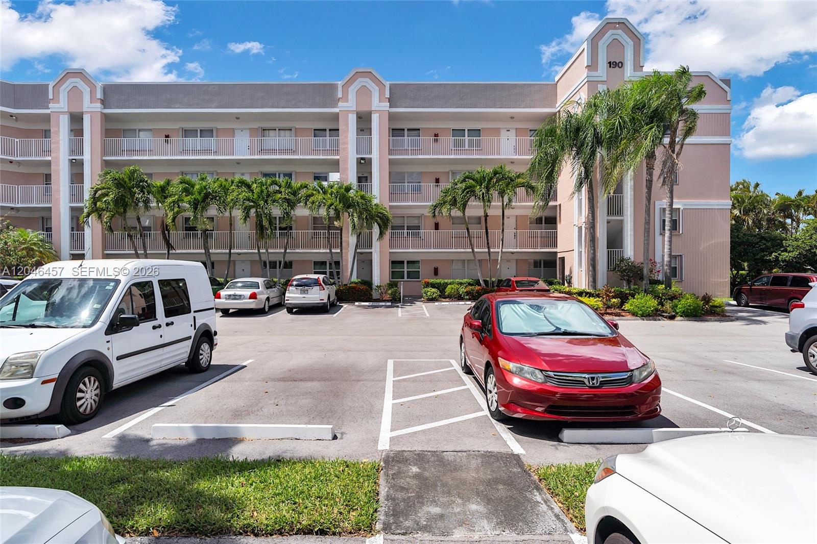 A multi-story pink apartment building features balconies and a parking lot with several cars — 2603 NW 103rd Ave # 310, Sunrise FL 33322, SUNRISE, FL