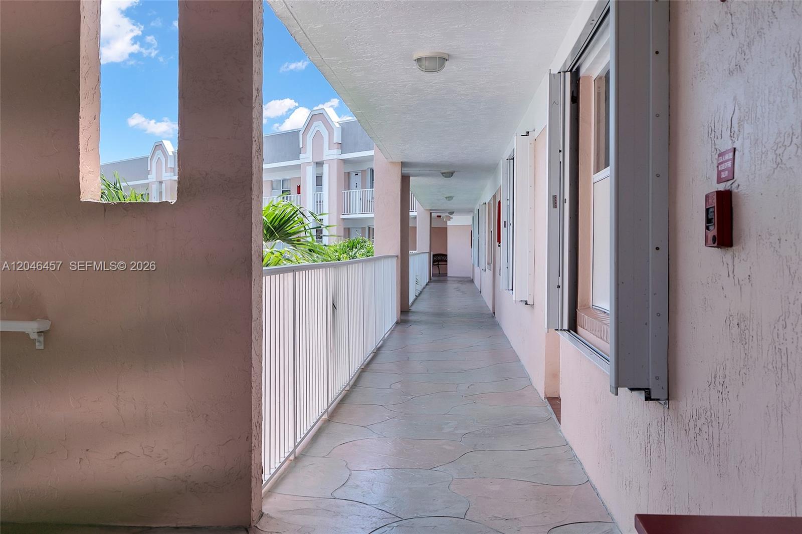 An outdoor apartment building walkway features a white metal railing and light-colored tiled flooring — 2603 NW 103rd Ave # 310, Sunrise FL 33322, SUNRISE, FL