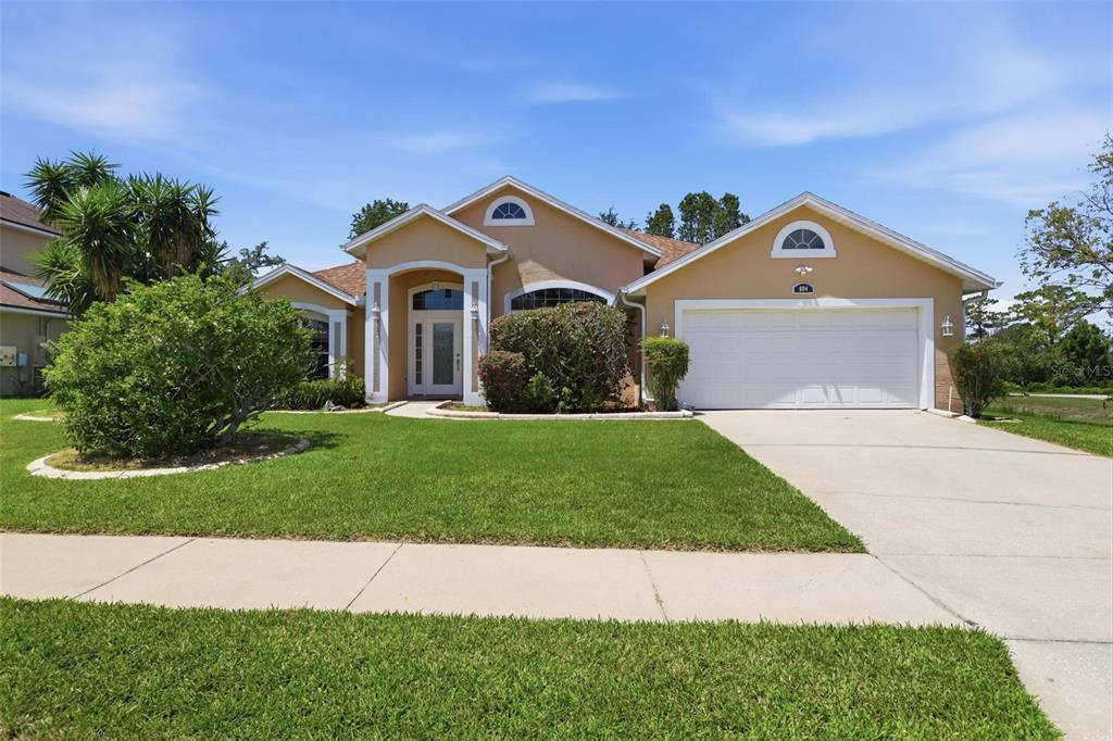 A single-story suburban house with a tan stucco exterior, a two-car garage, and a lawn — 694 SHAWSBURY WAY, DELTONA, FL