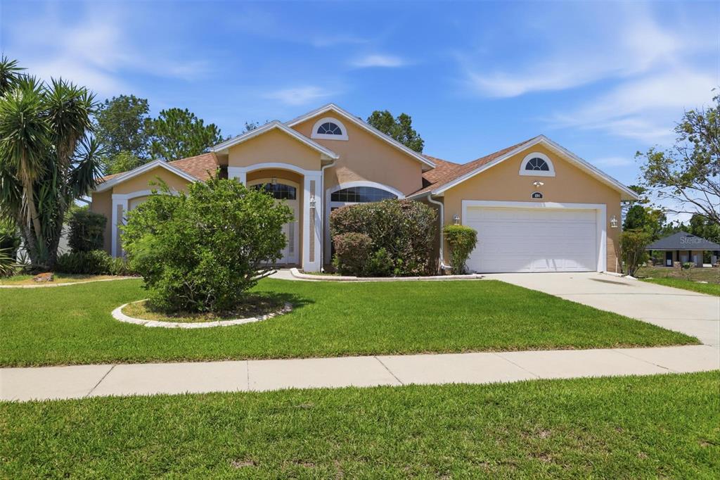 A single-story tan house with a two-car garage and a landscaped front lawn — 694 SHAWSBURY WAY, DELTONA, FL
