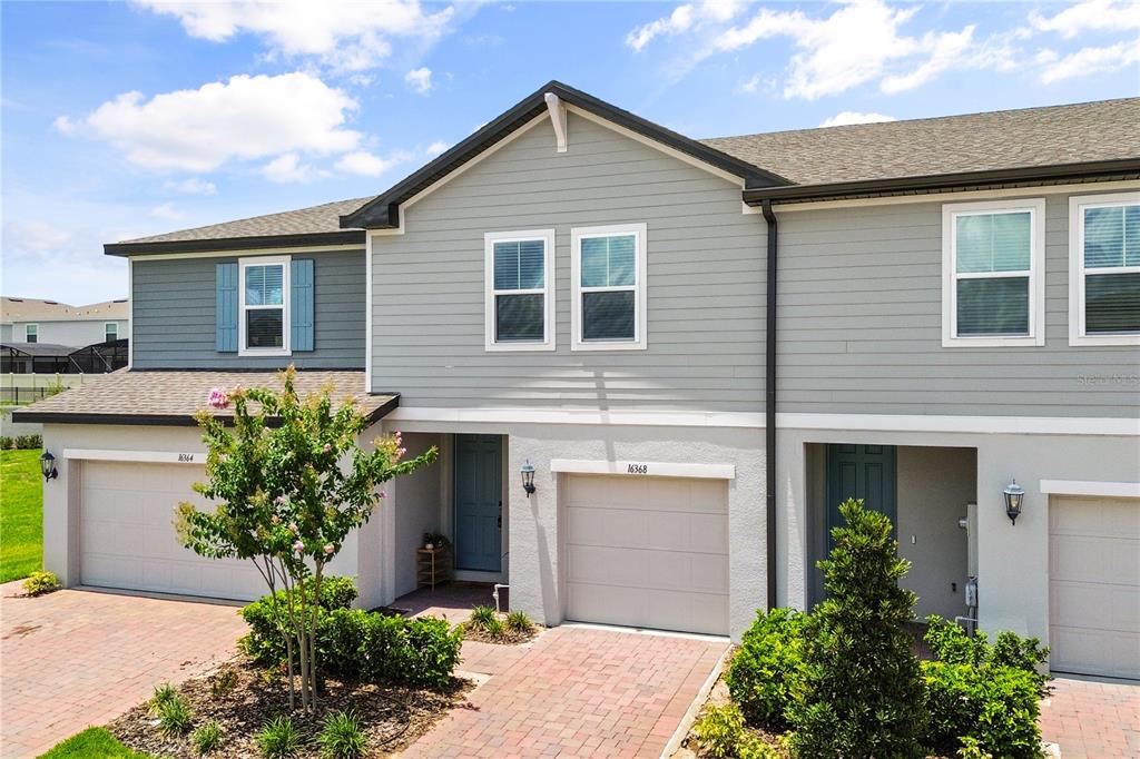 A two-story townhouse exterior with gray siding, a brick paver driveway, and two garage doors — 16368 HAPPY EAGLE DRIVE, CLERMONT, FL