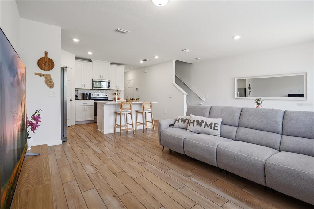 A living room with wood-look tile floors flows into a kitchen featuring white cabinets — 16368 HAPPY EAGLE DRIVE, CLERMONT, FL
