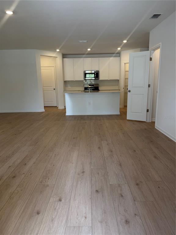 An open-concept kitchen features white cabinets, stainless steel appliances, and light wood-look flooring — 5176 CLAY WHALEY ROAD, ST CLOUD, FL