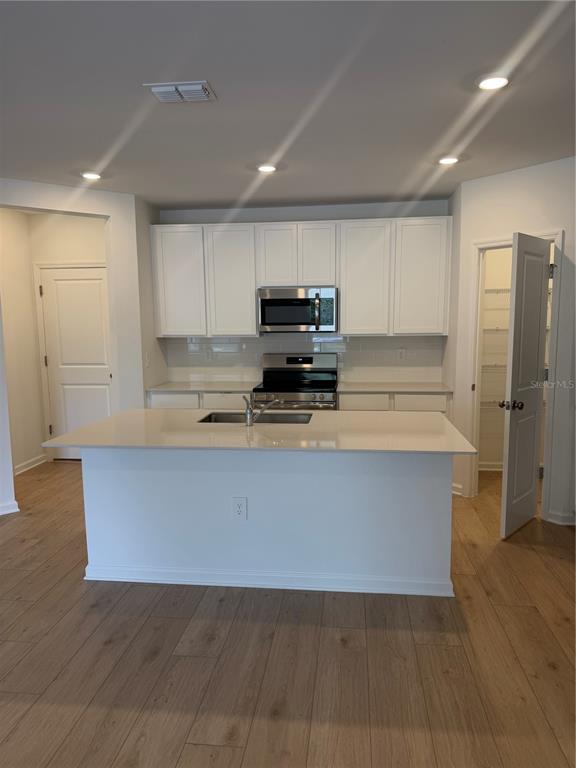 A kitchen features white cabinets, stainless steel appliances, a central island, and light wood flooring — 5176 CLAY WHALEY ROAD, ST CLOUD, FL