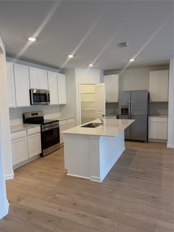A kitchen features white cabinetry, stainless steel appliances, a center island, and wood-look flooring — 5176 CLAY WHALEY ROAD, ST CLOUD, FL