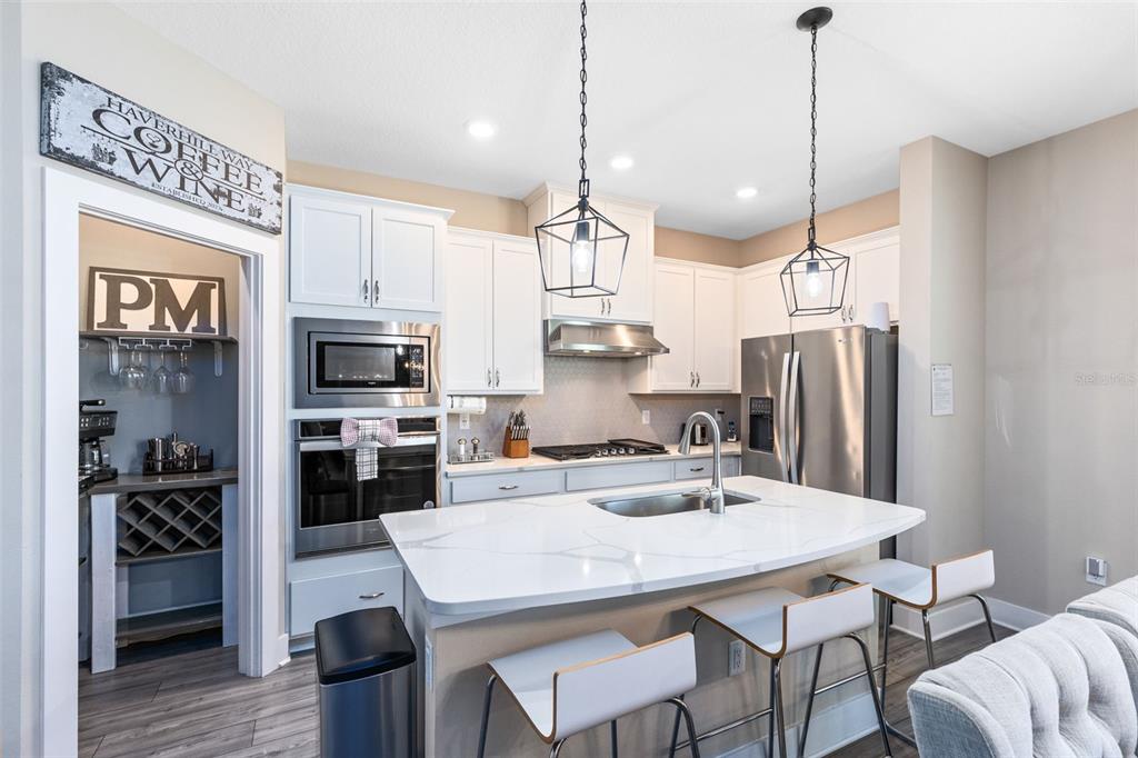 A modern kitchen features white cabinets, a quartz-topped island with bar seating, and stainless appliances — 7962 HAVERHILL WAY, REUNION, FL