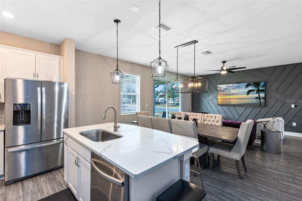 A kitchen island with a sink faces a dining area featuring a geometric accent wall — 7962 HAVERHILL WAY, REUNION, FL