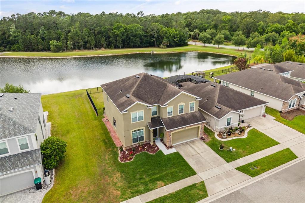 An aerial view shows a two-story suburban house with a garage next to a lake — 10536 CABBAGE TREE LOOP, ORLANDO, FL