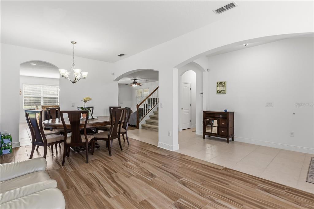 A dining area with wood-look tile flooring connects to a tiled entryway and staircase — 10536 CABBAGE TREE LOOP, ORLANDO, FL