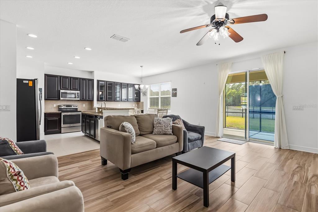 An open-concept living room and kitchen featuring wood-look tile flooring and a sliding glass door — 10536 CABBAGE TREE LOOP, ORLANDO, FL