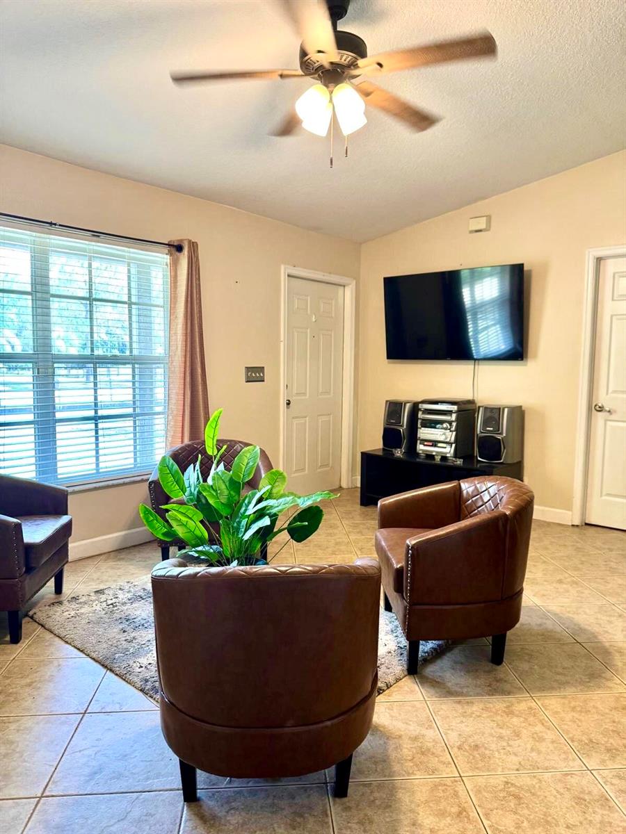 A living room features tile flooring, a ceiling fan, three brown armchairs, and a television — 16298 90th Street N, FL 33470, FL